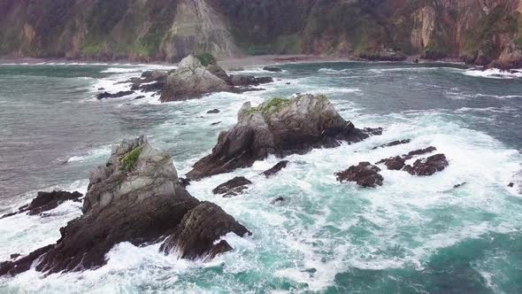 Ocean and Giant Waves Crashing at Rocky Cliff with Splashing and White Foam