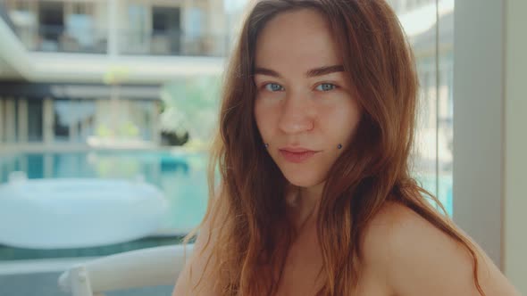 Young Woman with Brown Hair and Beautiful Brown Eyes Sitting in the Hotel Courtyard Smiling