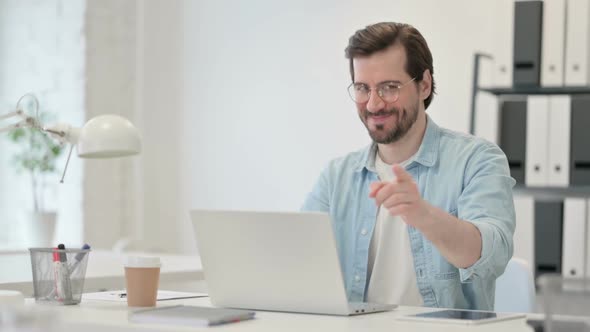 Young Man with Laptop Pointing at Camera