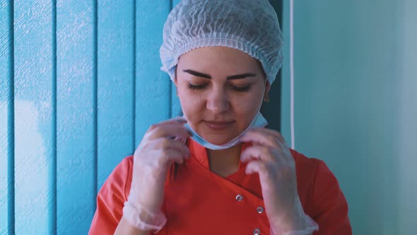 Medical Worker in Uniform and Cap Puts on Protective Mask