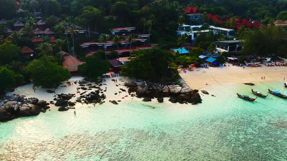 An aerial shot of unrecognisable people walking along the beach and resorts in the background.
