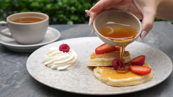 Woman Hand Pouring Maple Syrup on American Pancakes with Fresh Berries