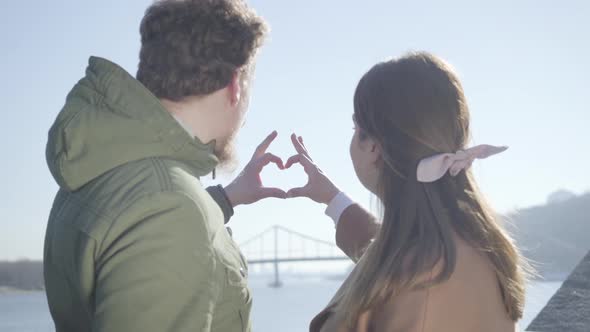 Close-up of Young Man and Woman Making Heart Shape with Hands. Couple in Love Looking at Each Other