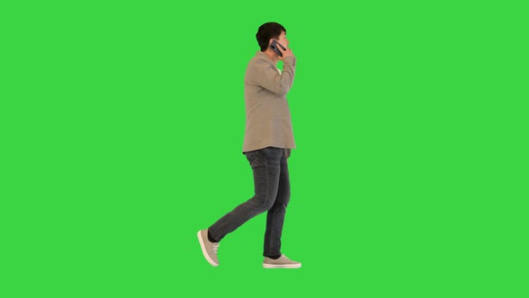 Young Asian Man Walks Talking on His Smartphone and Smiling on a Green Screen Chroma Key
