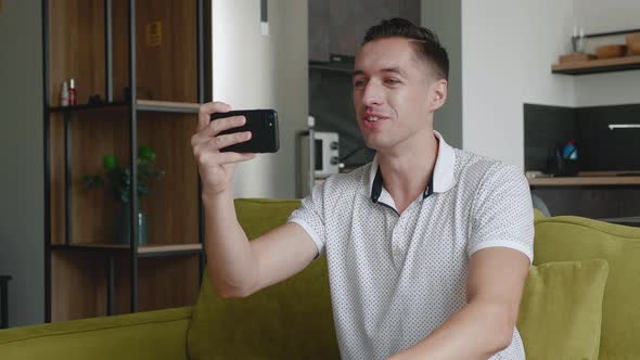 Smiling Young Man Making Video Call While Sitting on a Couch at Home. Portrait of Male Doing a Video