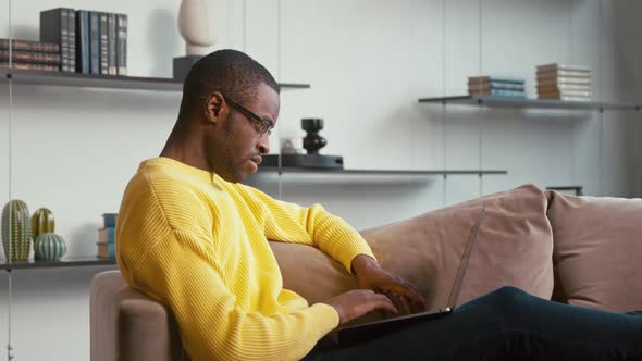 Serious man in glasses typing on laptop keyboard sitting on sofa