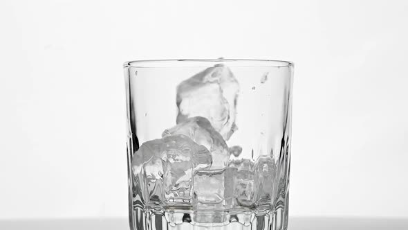 Ice cubes fall in empty whiskey glass over white