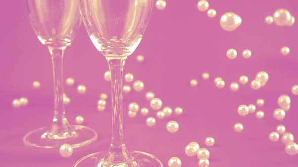 Falling white pearls next to wine glasses on a purple background. Slow motion.