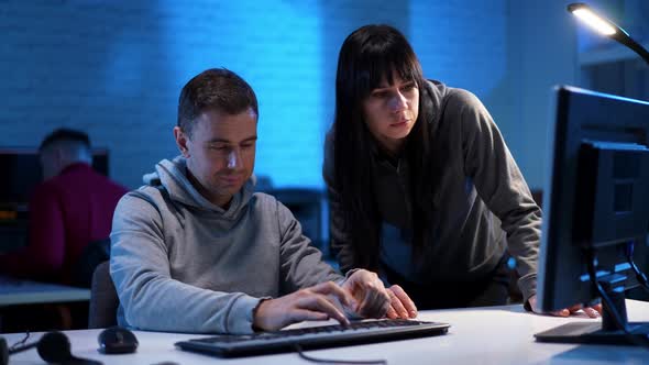 Beautiful Young Woman Approaching Colleague Coding Programming at Table in Blue Office