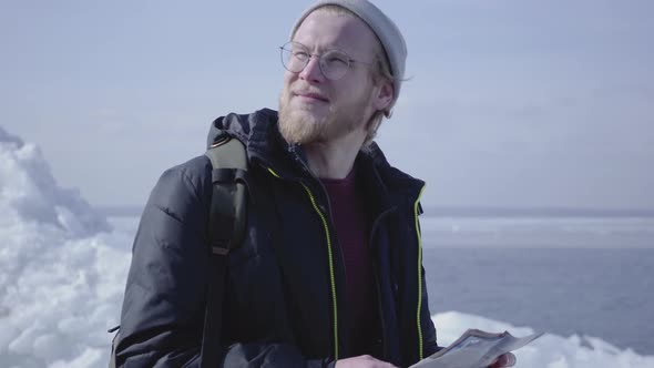 Portrait of Young Blond Bearded Handsome Man Wearing Warm Jacket and Hat Walking on the Glacier