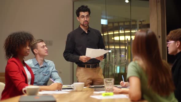 Multiethnic Startup Business Team Sitting at Table Listen to Report of Colleague Making Speech at