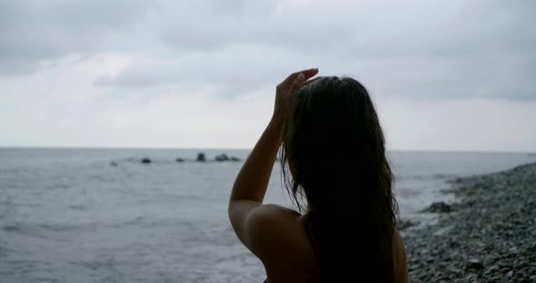 Pretty Lady with Long Wet Hair Meditates on Rocky Beach