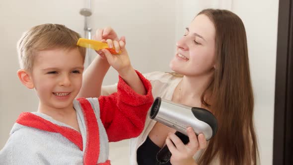 Young Caring Mother Drying Hair and Looking on Her Little Son in Bathroom