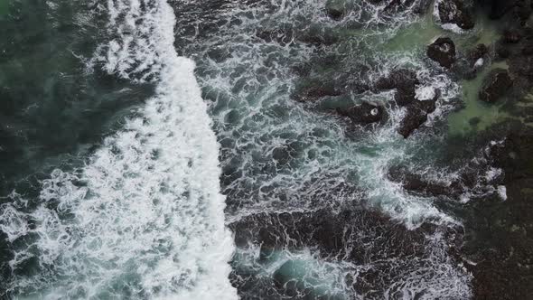 Top down aerial view of giant ocean waves crashing and foaming in coral beach