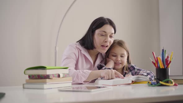 Portrait of Happy Caucasian Mother Reading Book for Daughter and Kissing Her Head. Positive