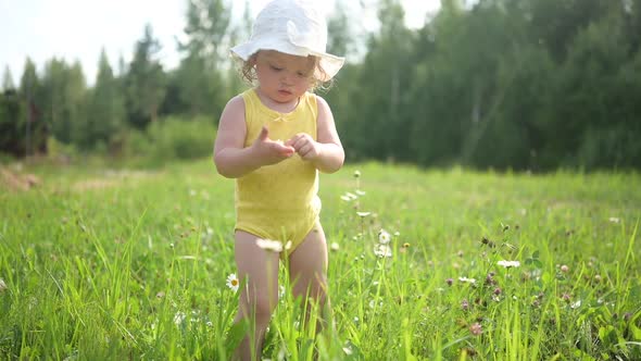 Little Funny Cute Blonde Girl Child Toddler in Yellow Bodysuit and White Hat Walking in Field with