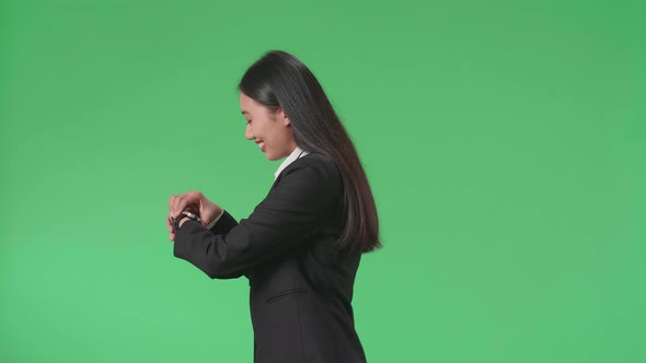 Side View Of A Smiling Asian Business Woman Looking At A Watch While Walking Through Green Screen