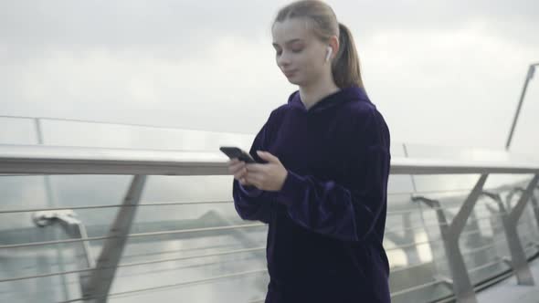 Smiling Beautiful Young Sportswoman Jogging and Using Smartphone Outdoors