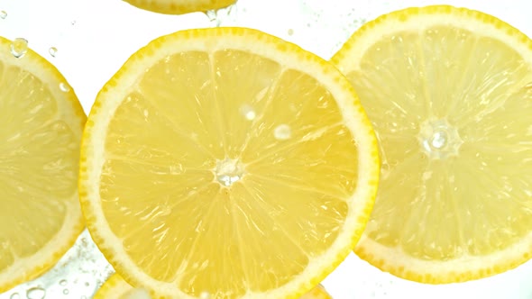 Super Slow Motion Shot of Lemon Slices Falling Into Water on White Background at 1000Fps.