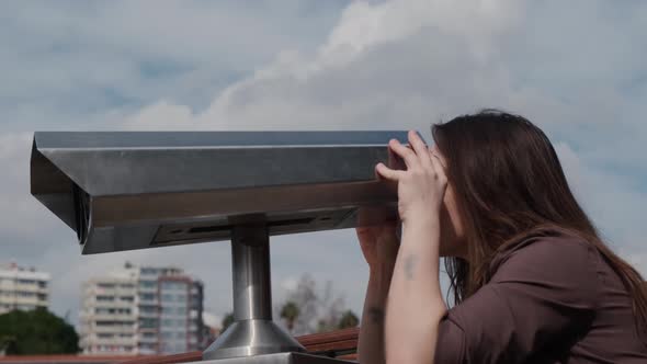 Girl traveler looks through sightseeing binoculars at sights in tourist country.