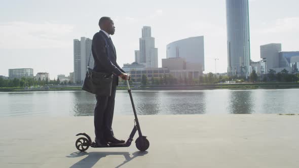 Afro Businessman Riding On E-Scooter Along River