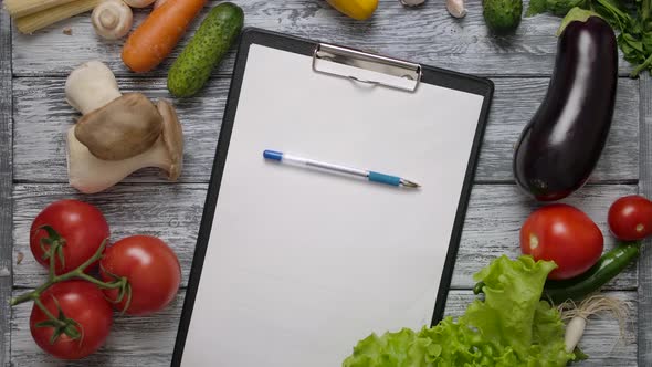 Pen Rolling on Blank Clipboard on Kitchen Table with Vegetables