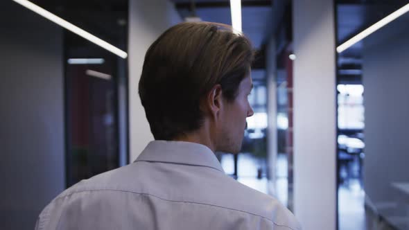 Rear view of caucasian businessman walking through office corridor holding smartphone