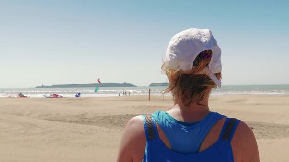 Tourist girl watching a beach full of kite surfers on sunny day, Morocco