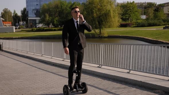 Portrait of a Businessman on a Gyroscope with a Phone in a Park in Sunny Weather