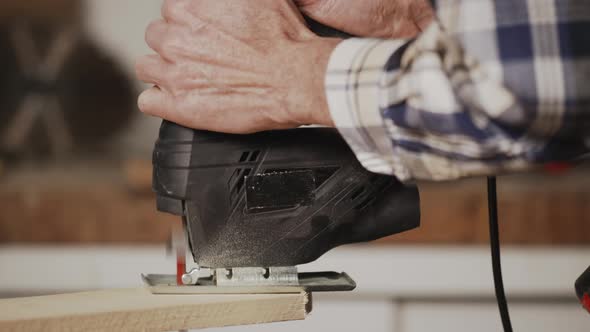 Carpenter is Sawing a Wood Plank with Electric Jig Saw Machine in Carpentry Workshop