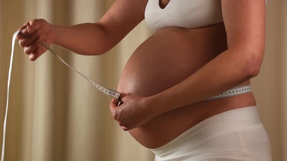 Pregnant woman checking her belly with tape measure