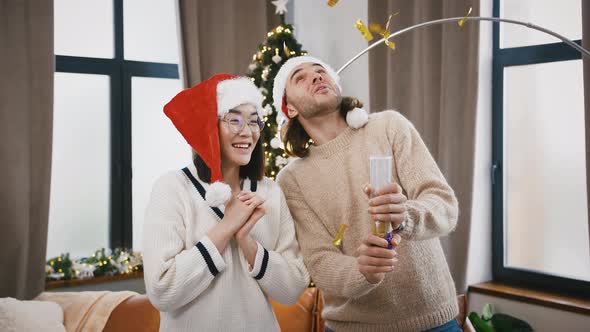 Multiracial Couple Laughing Blowing Up a Party Cracker Golden Confetti Flying Out Decorated