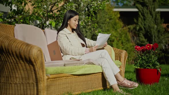 Young Professional Asian Woman Sitting in Sunny Garden Examining Business Graphs