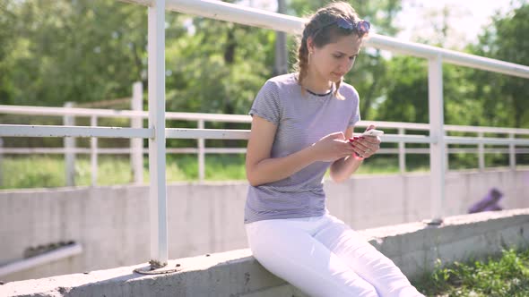 Attractive Young Woman Uses Smatphone in Park at Day