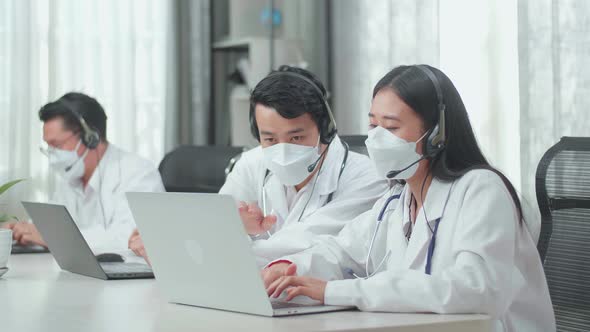 A Man And A Woman Of Three Asian Doctors In Mask Working As Call Centre Agent Discussing Work