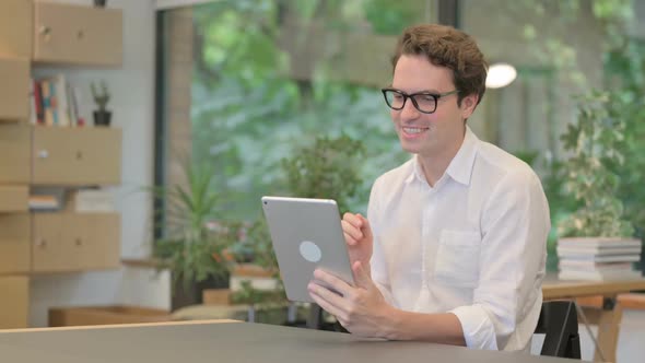 Young Man Celebrating Success on Tablet in Modern Office