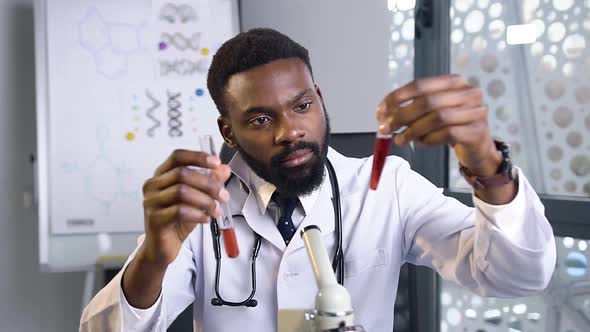 African American Medical Worker Comparing Two Test Tubes with Liquids in the Hospital Laboratory