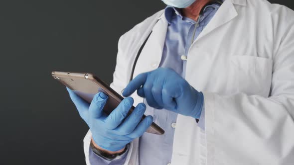 Mid section of caucasian male doctor wearing surgical gloves using digital tablet