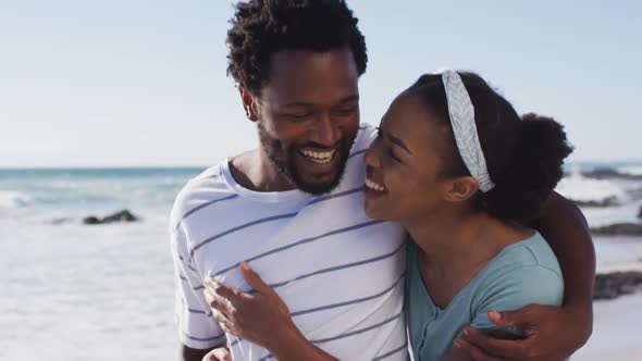 African american couple smiling, embracing and walking on the beach