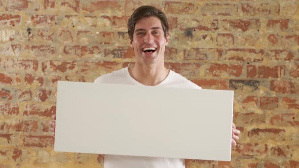 Caucasian man holding a white rectangle on a brick wall