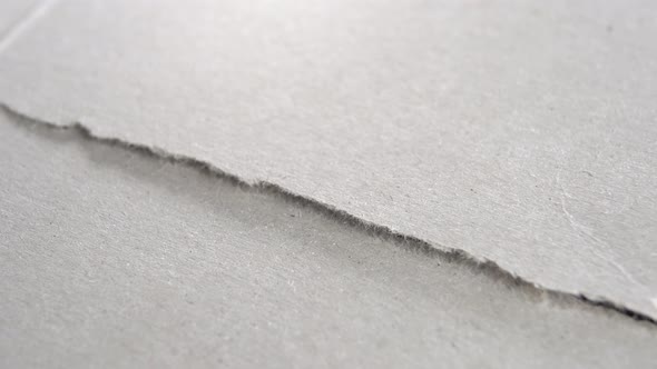 Torn grey paper edge. Ripped cardboard layers. Macro. Rotation. Grunge gray surface