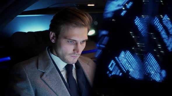 Portrait of a Young Businessman Sitting in a Moving Car and Using Laptop Man Top Manager in a Suit