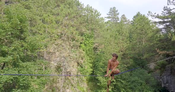 A man tries to balance while slacklining on a tightrope in the mountains.