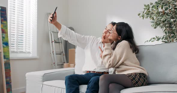 A Married Couple Freshly Moved Into a Purchased Apartment are Sitting on the Couch Hugging the Man