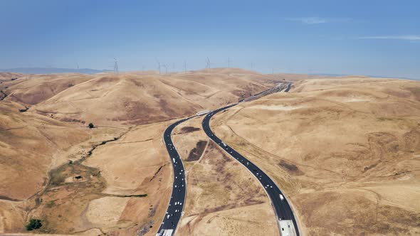 Busy Traffic Along a Winding Road Among Golden Hills. Wind Generators Are Visible in a Distance alt