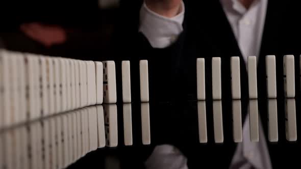 Businessman Hand Stopping Dominoes Row From Falling on a Black Mirror Background