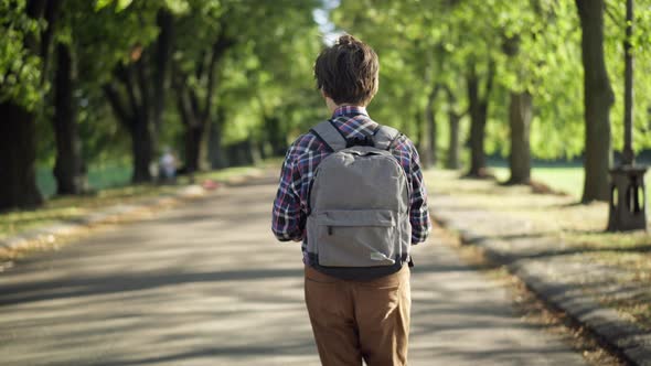 Tracking Shot of Confident Intelligent Teenage Boy with Backpack Walking in Sunshine in Summer Park