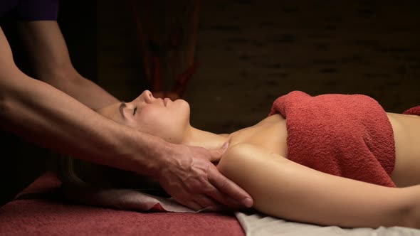 A man masseur kneads the shoulders of a young woman on a massage table