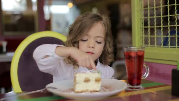 Funny little girl hiding behind white table and looking at tasty cake