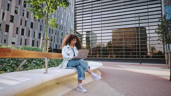 Outdoors Portrait of African American Girl with Afro Hairstyle Sitting Outdoors on Street in the